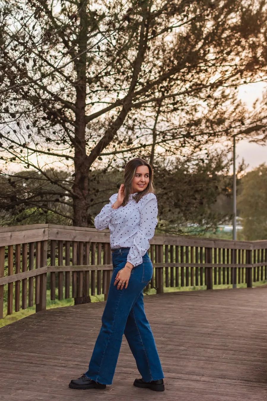 Ana Paula Maia, psicóloga, ao ar livre em uma ponte de madeira ao entardecer